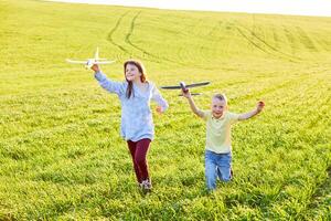 alegre y contento niños jugar en el campo y imagina sí mismos a ser pilotos en un soleado verano día. niños Sueños de volador y aviación. foto