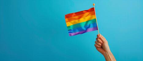 A hand holding rainbow flag isolated on blue background, pride month celebration photo