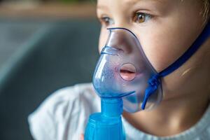 Close up view of little girl are sitting and holding a nebulizer mask leaning against the face, airway treatment concept photo