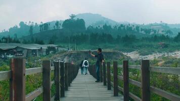 Person standing on a wooden bridge with a scenic view of lush green hills and overcast sky in the background. video