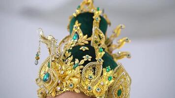 Close-up of an ornate golden crown with emerald accents on a blurred background. video