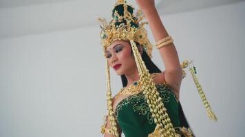 Elegant woman performing traditional dance in ornate costume with golden headdress against a plain background. video