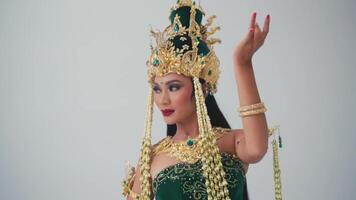 Woman in traditional Balinese costume with golden headdress and jewelry, performing a dance gesture. video