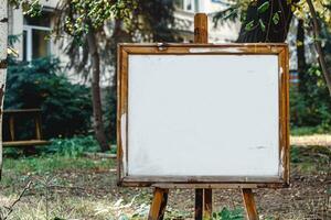 An empty whiteboard placed on a wooden easel outside among trees photo