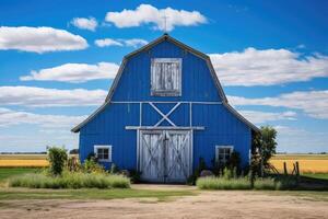 A classic blue barn with white trim located amidst a vast countryside landscape under a blue sky with clouds photo
