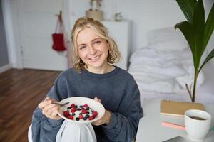 Cute girl eats breakfast and drinks tea in her room, makes herself healthy lunch in bowl, sits in bedroom photo