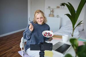 Portrait of young woman vlogger, recording herself while eating homemade healthy breakfast, creating vlog content for followers photo