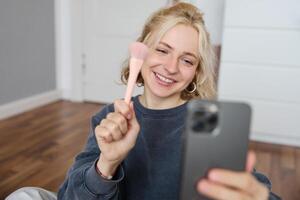 Portrait of young woman, social media influencer, taking selfies in her room, sitting on floor, holding smartphone and posing for a photo