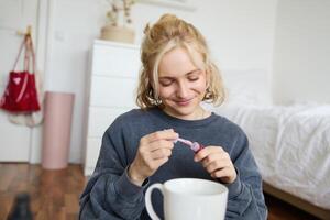 retrato de sonriente carismático mujer, pone en labio brillo, bebidas té, registros en digital cámara, belleza contenido para social medios de comunicación cuenta foto