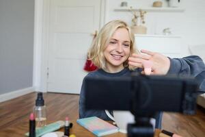 Close up portrait of happy young beauty blogger, records lifestyle vlog in her room, using camera with stabiliser, shows makeup brush and cosmetics photo