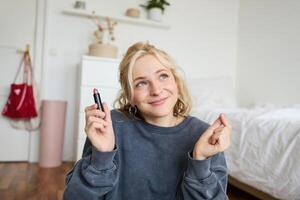 Portrait of cute, charismatic beauty blogger, woman sits in a room with lipstick in hand, talking about makeup, chatting with followers, recording online stream on social media app photo