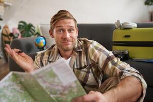 imagen de encogiéndose de hombros hombre con la carretera viaje mapa, mira a cámara con confuso rostro, paquetes maleta para día festivo, planes un viaje foto