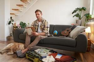 Portrait of man sitting with his dog, packing suitcase for a holiday, going on trip with a pet photo