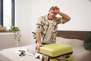 Portrait of man struggling to close suitcase full of clothes, putting effort to pack luggage for holiday, going on long vacation with lots of things photo