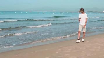 knap tiener jongen wandelingen langs de kustlijn gebruik makend van smartphone Aan zomer weekend vakantie.geniet sociaal media gebruik makend van mobiel telefoon concept.hoog kwaliteit full HD beeldmateriaal video