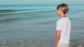 ein Teenager steht auf das Strand und sieht aus in das Distanz, genießen das Meer Luft und das Wellen Ansicht, Salou Stadt Spanien, sonnig Tag.Familie Ferien, Urlaub, Reise, Reisen Konzept.langsam Bewegung ,schließen oben ,Seite Aussicht Clip.hoch Qualität fullhd Aufnahmen video