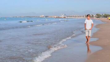 gut aussehend Teenager Junge im Weiß T-Shirt Spaziergänge entlang das Küste genießen Sommer- Wochenende Urlaub, Salou Stadt Spanien.Hoch Qualität fullhd Aufnahmen video