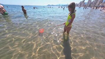 Benidorm, España -junio 22,2023. niña con un pescar savia molesto a captura un tropical pescado.playa lleno de gente, levante playa benidorm ciudad, españa. lado ver clip.alto calidad 4k imágenes video