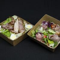 Salads with meat in paper plates on black background photo