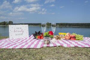 hermosa picnic con frutas, vegetales y lentes de vino cerca lago. foto