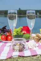 Beautiful picnic with fruits, vegetables and glasses of wine near lake. photo