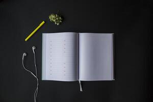 Opened planner with pen and head phones on the black table. Modern workplace. Background with copy space. photo