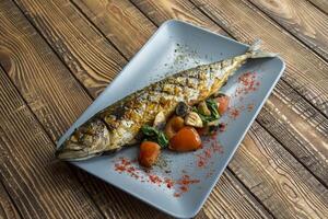 Grilled fish with vegetables in a plate on a wooden table. photo