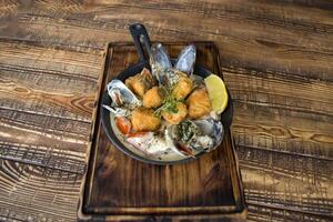 Fried fish with mussels, sauce and lemon on a wooden table. photo