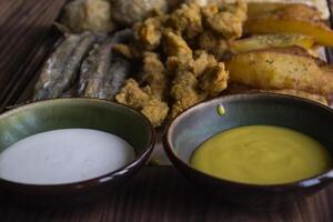 Fried potatoes with fish, cheese sticks and sauces. photo