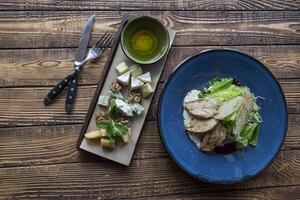 The hot salad with meat, and cheese plate on a wooden table. photo