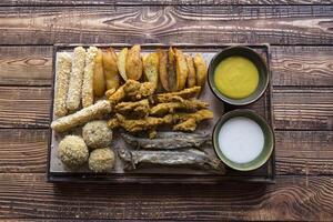 Fried potatoes with fish, cheese sticks and sauces. photo