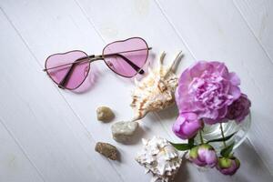 Pink glasses, peonies and sea shells on a white wooden table. Romantic summer flat lay. photo