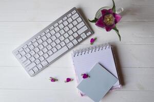 Computer keyboard and notebook with empty sheet. Modern workplace. photo