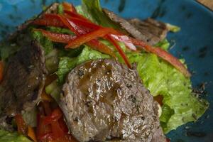 The salad with warm veal and oyster sauce in a plate on the wooden table. photo