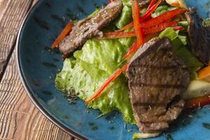 The salad with warm veal and oyster sauce in a plate on the wooden table. photo