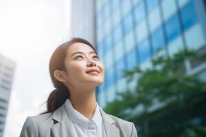 Happy young Asian business woman standing on street outside modern office building in the city. Portrait of professional businesswoman. Office worker looking up to the sky and smiling photo