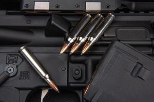 Close-up of .223 carbine cartridges. Loaded weapon clip. Weapons in the back photo