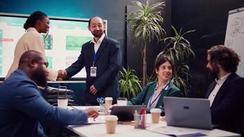 project manager beven handen en feliciteren hun nieuwste medewerker, gastvrij haar naar zijn bedrijf team gedurende een zakelijke briefing in bestuurskamer. ondertekening een nieuw werk contract. camera b. video