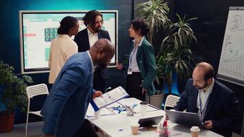 Team of startup colleagues preparing their presentation speech in front of the interactive board. Office employees meeting in a boardroom to review performance metrics as a group. Camera B. video