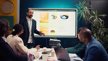 Management consultant gathering his employees for a status update meeting in boardroom, interactive presentation with the latest data. Success metrics and key performance indicators. Camera B. video