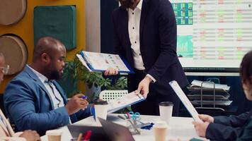 Team leader sharing clipboards with the latest performance metrics to discuss about work efficiency and optimization during corporate briefing meeting. Manager is consulting his personnel. Camera A. video