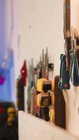 Vertical Chisels, screwdrivers, wrench and pliers on wall in furniture assembly shop next to electric router on workbench. Close up of woodworking gear on rack in joinery and power tool video