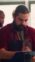 Vertical Craftsperson drawing blueprints on notepad in studio with BIPOC coworker in background solving tasks. Manufacturer looking at technical schematics to execute woodworking projects, camera A video