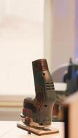 Vertical Close up of electric router on workbench in assembly shop with woodworking tools on rack in background. Focus on hand powered gear used for cutting wood in carpentry studio, panning shot video