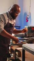 Vertical African american sculptor shaping raw timber using chisel and hammer in carpentry shop, creating wood art, wearing safety glasses. Artist making wood sculptures, engraving lumber with tools, camera B video