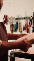 Vertical Carpenter inspecting wood in assembling shop, putting safety glasses on and picking tool from rack. Woodworking specialist in studio picking lumber block and carving gear for it, camera A video