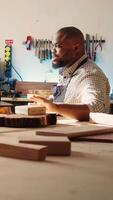 verticaal vrolijk fabrikant en leerling bespreken in studio naar selecteer het beste hout materialen voor project. vrolijk meubelmaker en collega pratend in schrijnwerkerij, aan het doen kwaliteit zekerheid Aan timmerhout, camera b video