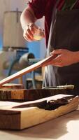 Vertical Woodworking specialist applying varnish on wood to build up protective layer. Cabinetmaker in assembly shop lacquering wooden board after sanding surface to ensure smoothness, close up shot, camera B video