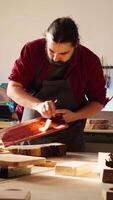 Vertical Carpenter in assembly shop starting restoration project on lumber block, applying lacquer on surface. Woodworking specialist coloring wood plank with paintbrush, doing handwork in studio, camera B video