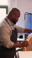 Vertical Carpenter in woodworking shop spinning wood block around, inspecting it before assembling furniture. BIPOC cabinetmaker in joinery studio evaluating lumber block, checking for damages, camera B video